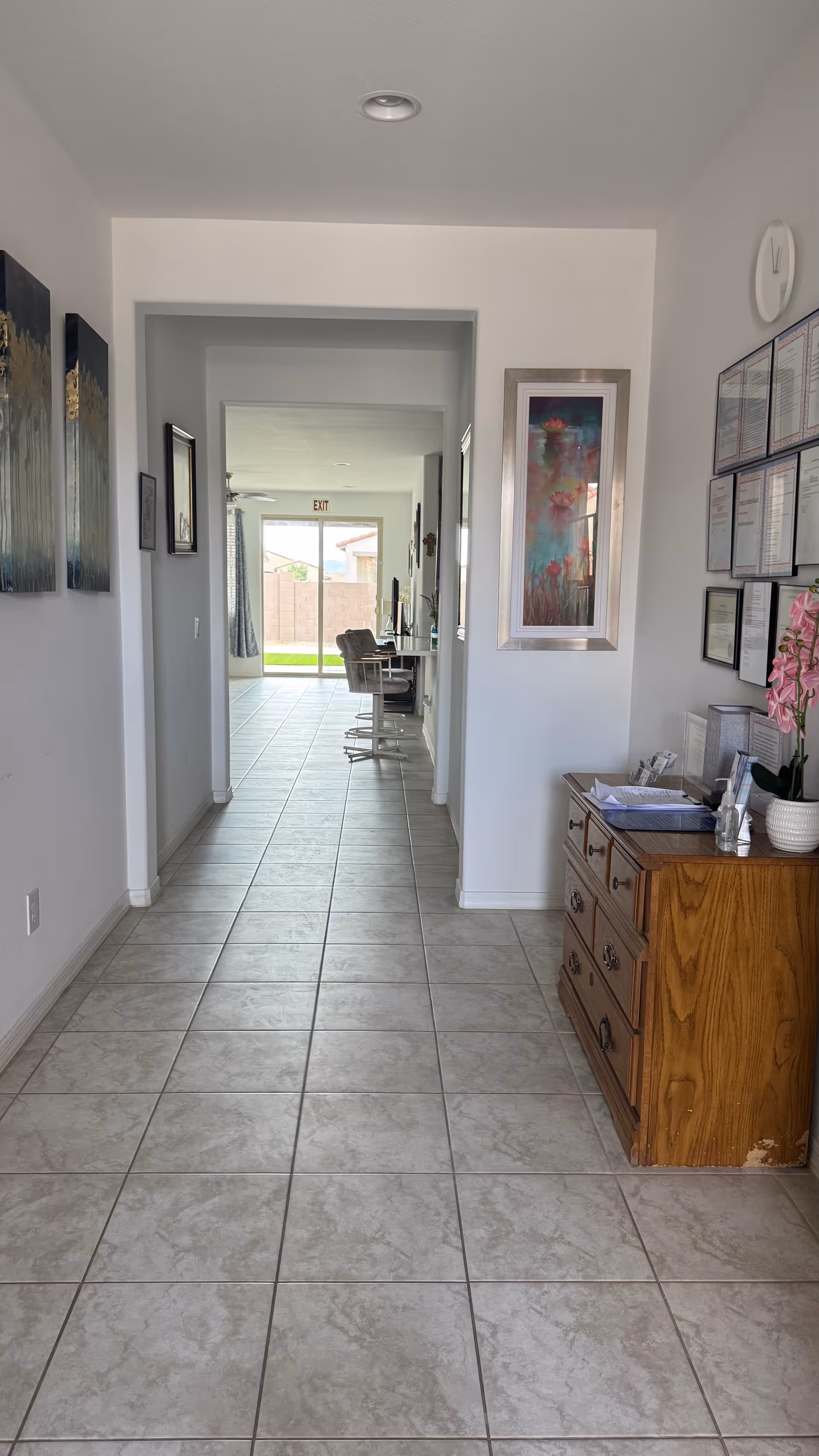 Long tiled hallway inside Caring Home Assisted Living with framed artwork and a wooden dresser.