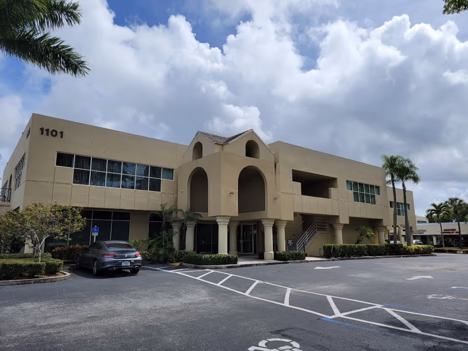 Beige two-story building with an arched entrance and a parking lot.