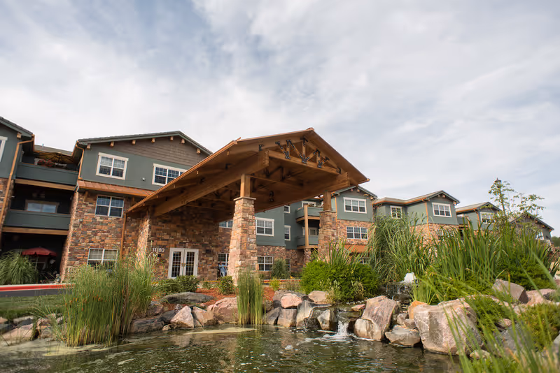 Exterior view of Keystone Place at Legacy Ridge, senior living facility with stone facade and pond.