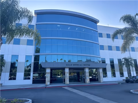 Modern medical center building with glass facade and palm trees at the entrance.