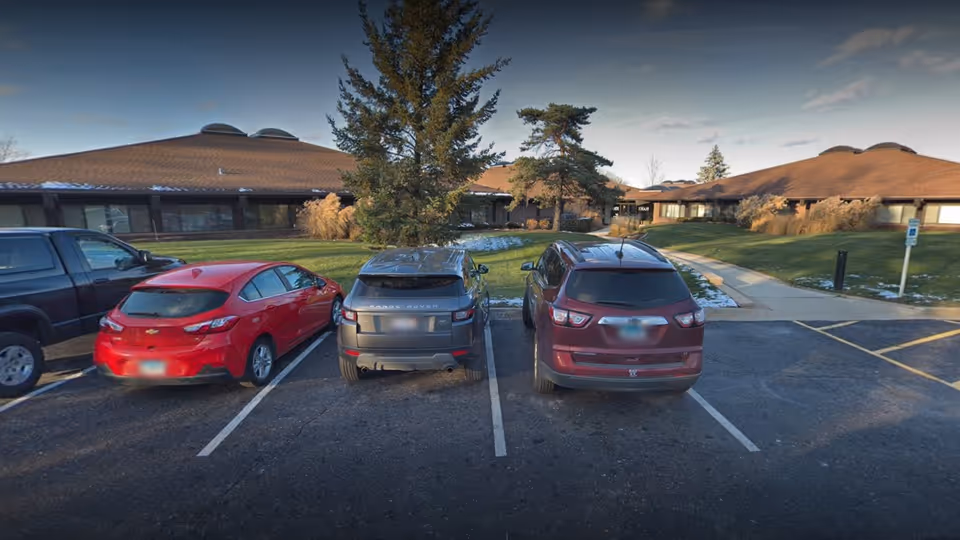 Parking lot in front of a single-story care facility with brown, sloped roofs.