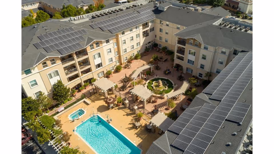 Aerial view of Heritage Estates' courtyard showing a swimming pool, spa, garden fountain, shaded seating areas, and solar panels on surrounding roofs.