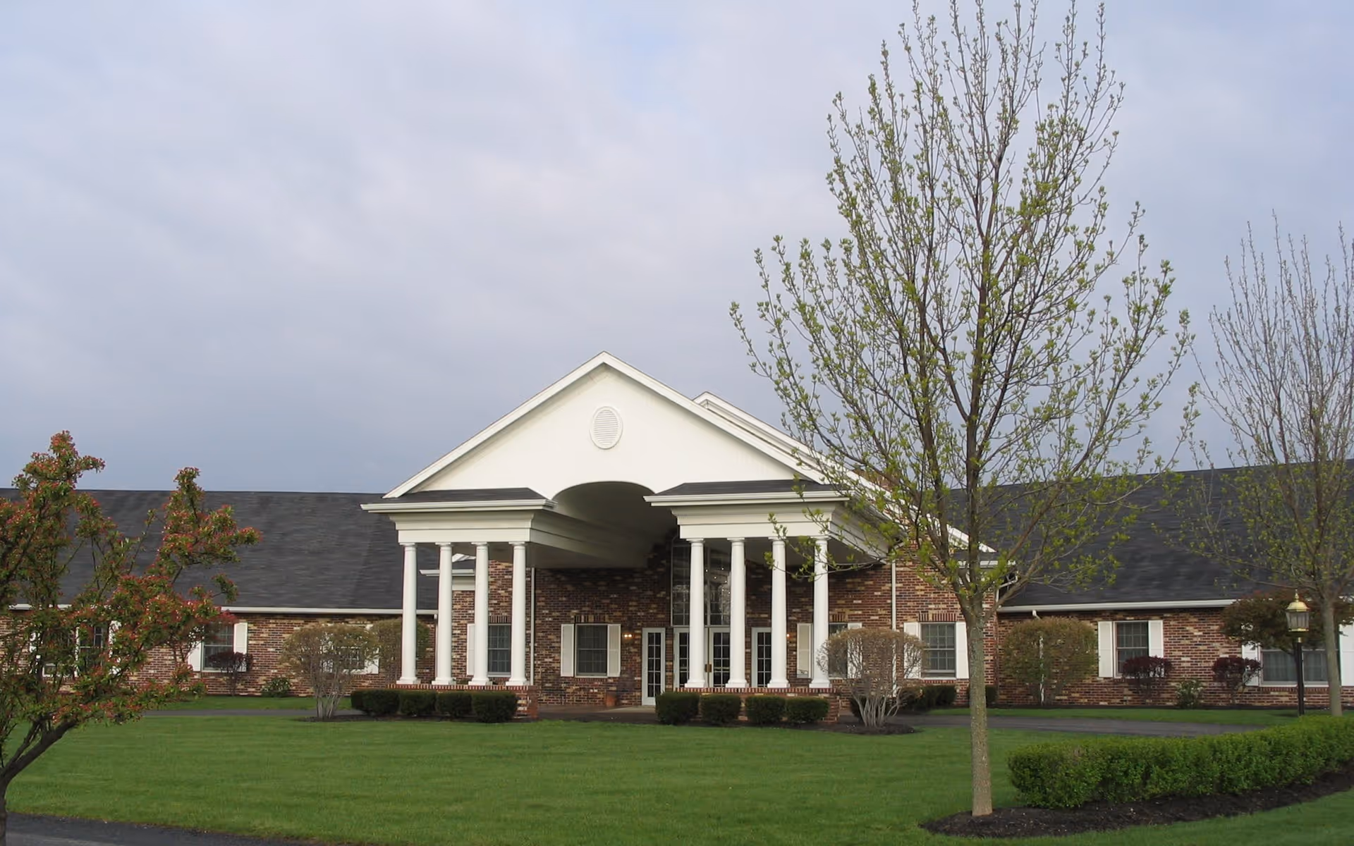 Brick senior living facility with a white-columned portico and manicured lawn.