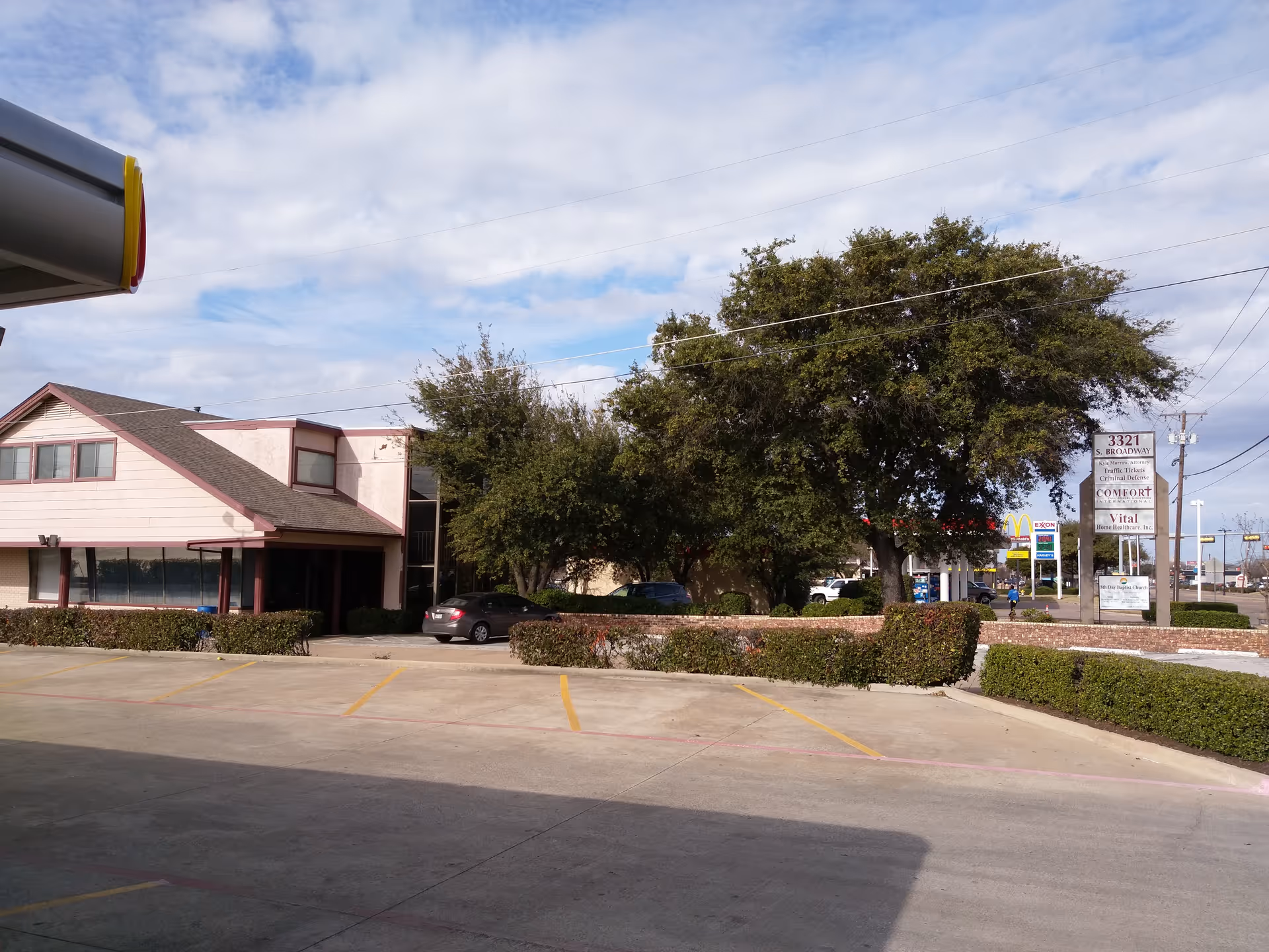 Exterior view of a senior care facility with a driveway, trees, and a sign.
