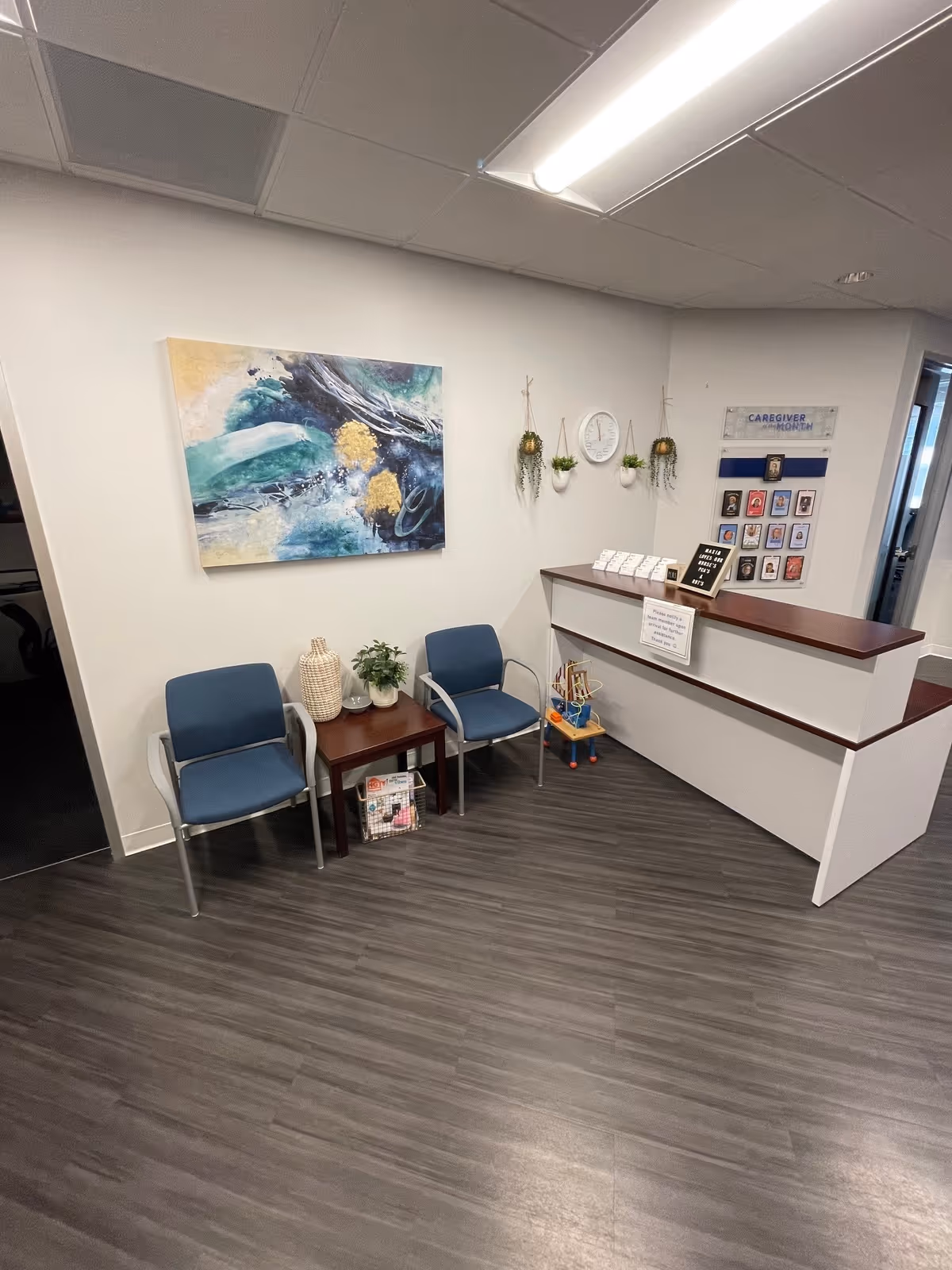 Reception area with blue chairs, a counter, wall art, and plants in a senior facility.