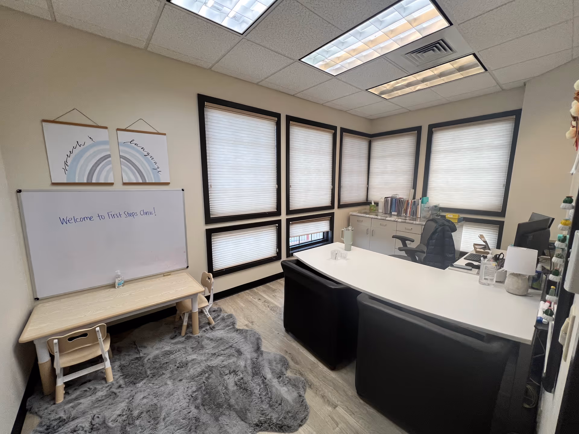 Reception area of a pediatric therapy clinic with a curved desk, whiteboard, and blinds.