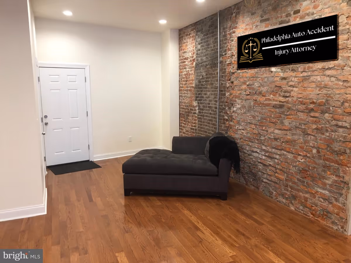 A modern interior with a brick accent wall, gray chaise, and wooden floor.
