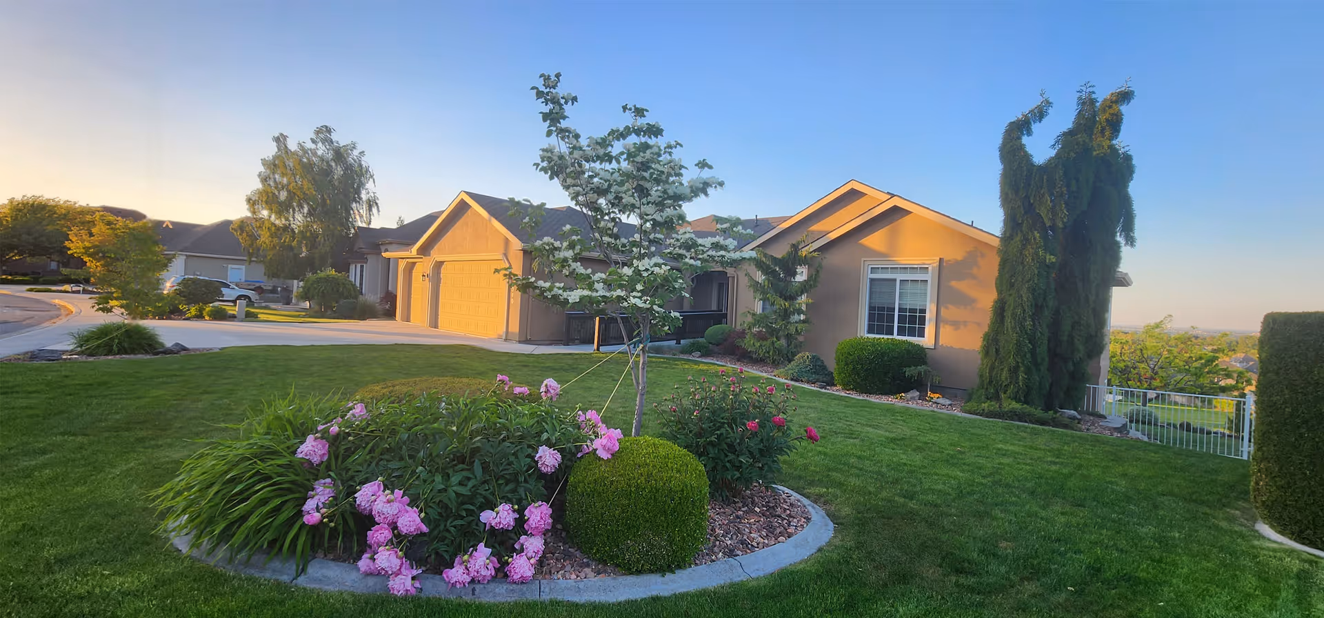 Front exterior view of a single-story senior living home with a well-kept lawn, flower beds, and a curved driveway.