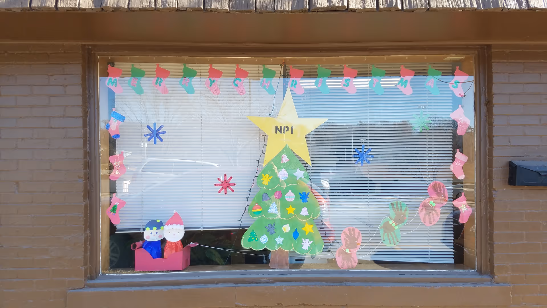 Brick building front window decorated with Christmas crafts and a paper tree.