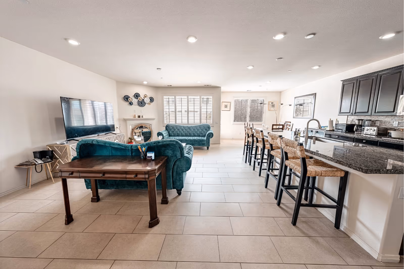 Bright open common area with teal sofas, TV, and bar-height kitchen seating.