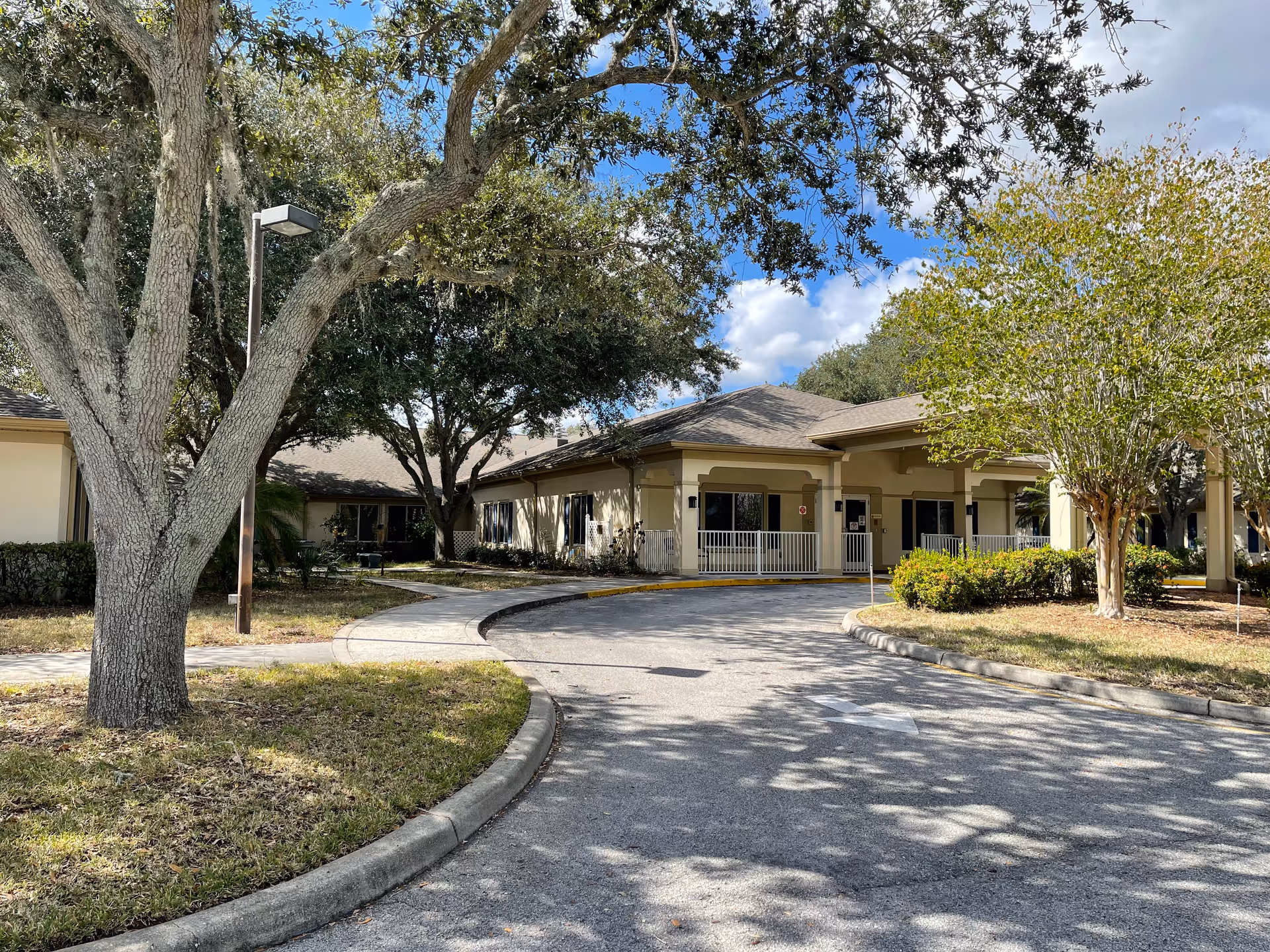 Exterior view of Consulate Health Care of Winter Haven with curved driveway and trees.