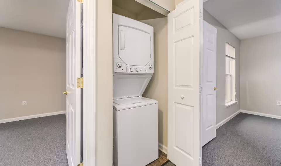 Stacked washer and dryer in a hallway laundry closet inside a senior living facility.