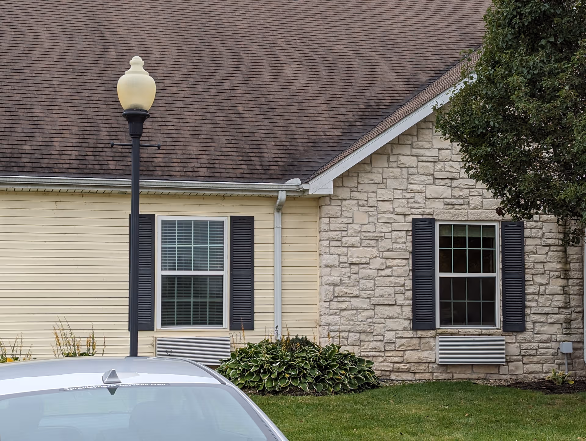Exterior view of Bickford of Champaign facility with beige siding, stone wall, windows, and street lamp.