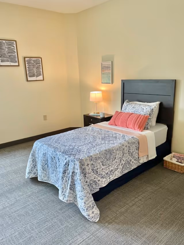 A neatly made bedroom in a senior living facility with a single bed and nightstand.