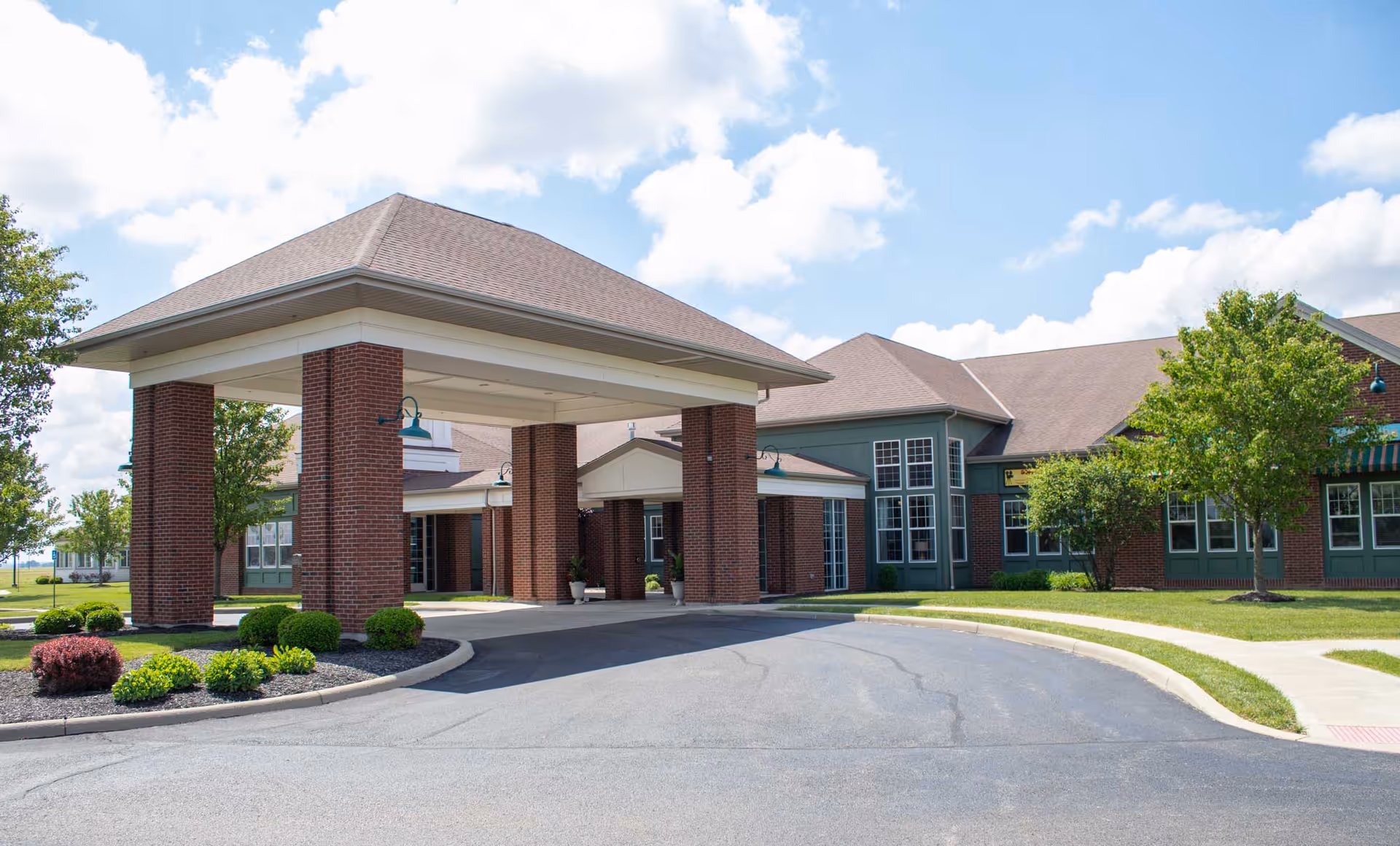 Exterior view of a senior living facility with a brick porte-cochere and landscaping