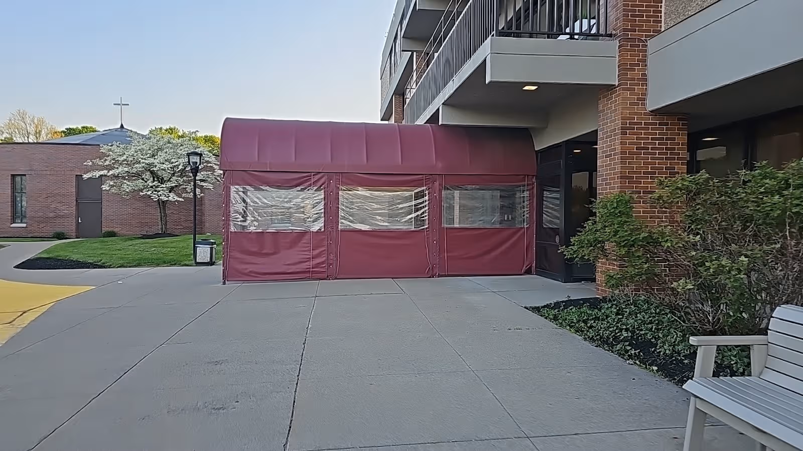 Exterior view of a brick senior living building with a maroon entrance tent.