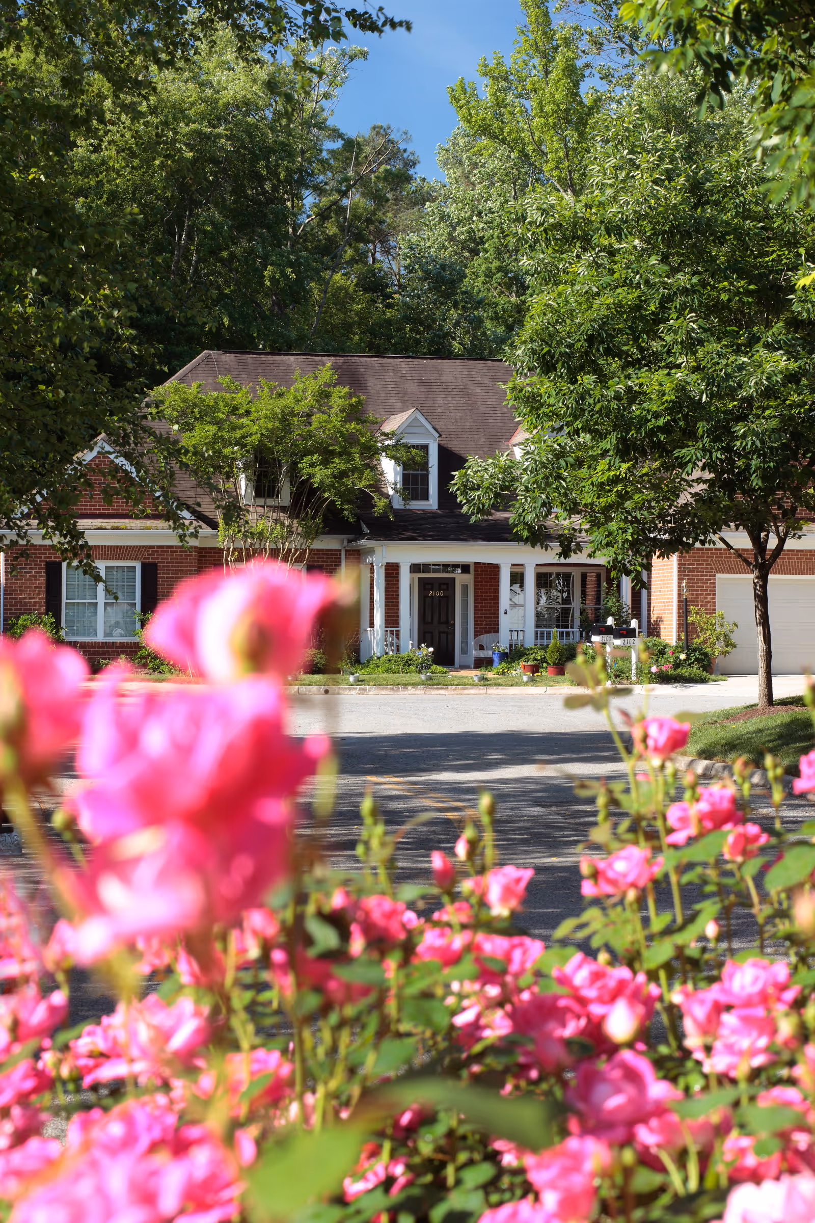 Brick residential building with a front porch and garage framed by pink flowers in the foreground.
