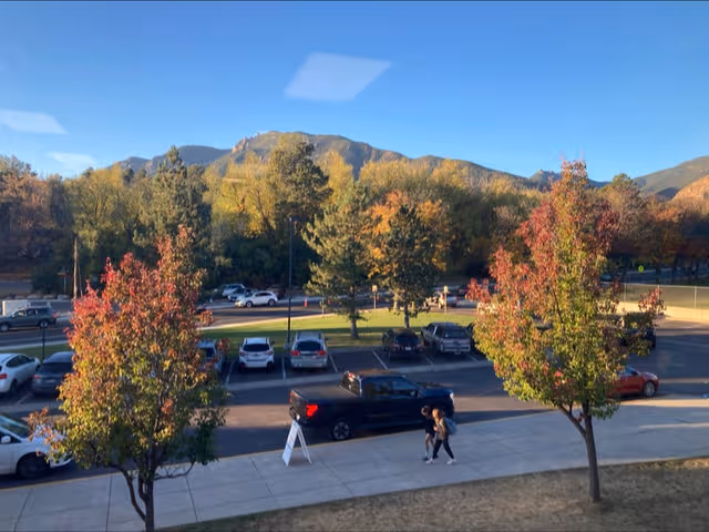 Parking lot with several cars, colorful trees, and distant mountains.