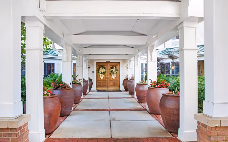 Covered entrance walkway lined with large terracotta planters leading to double wooden doors decorated with wreaths.