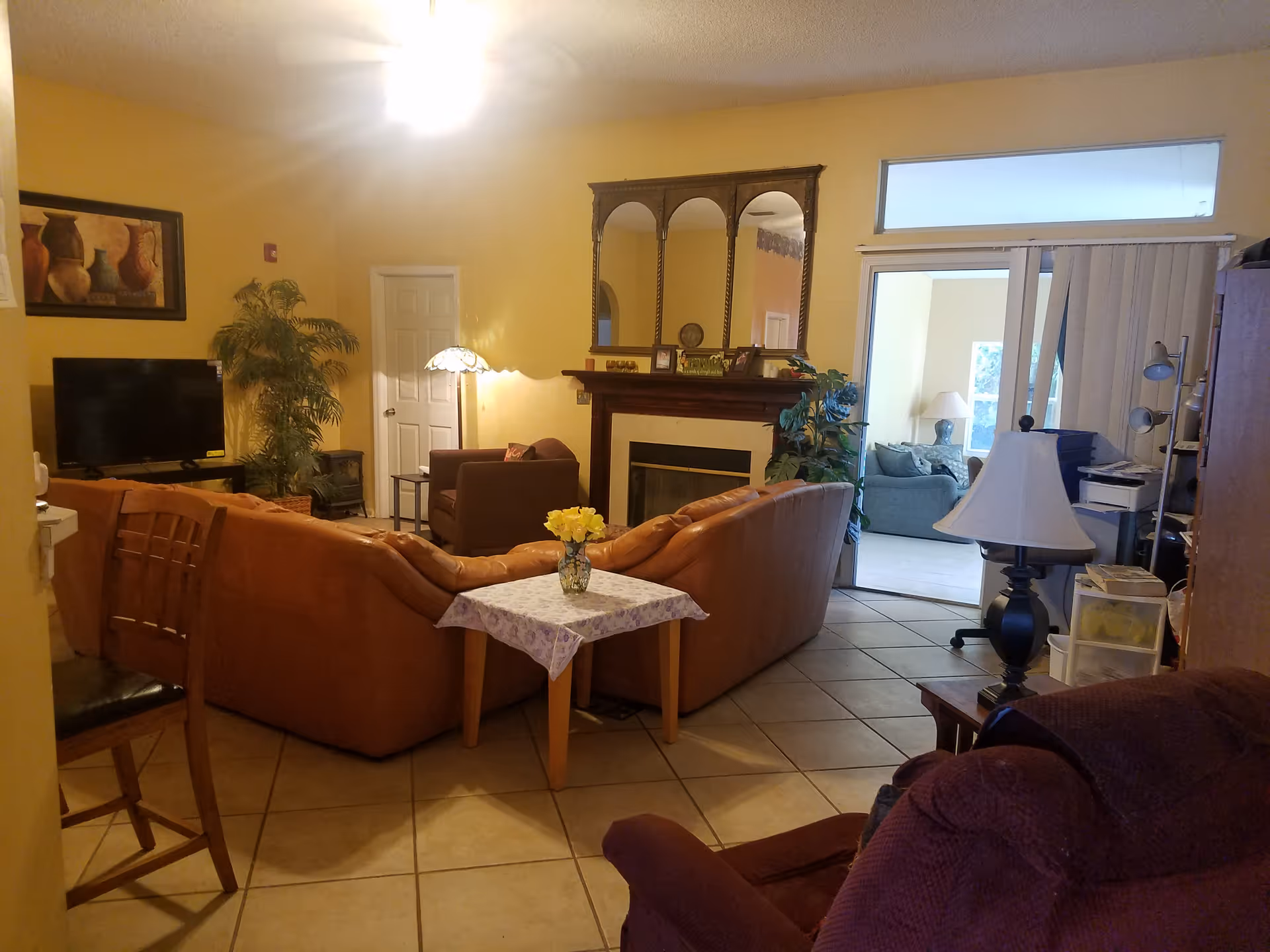 Spacious living room with tan sofas, a fireplace, plants, and a table with flowers.