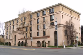 Exterior view of Marymount Villa, a beige, multi-story senior living building with trees nearby.