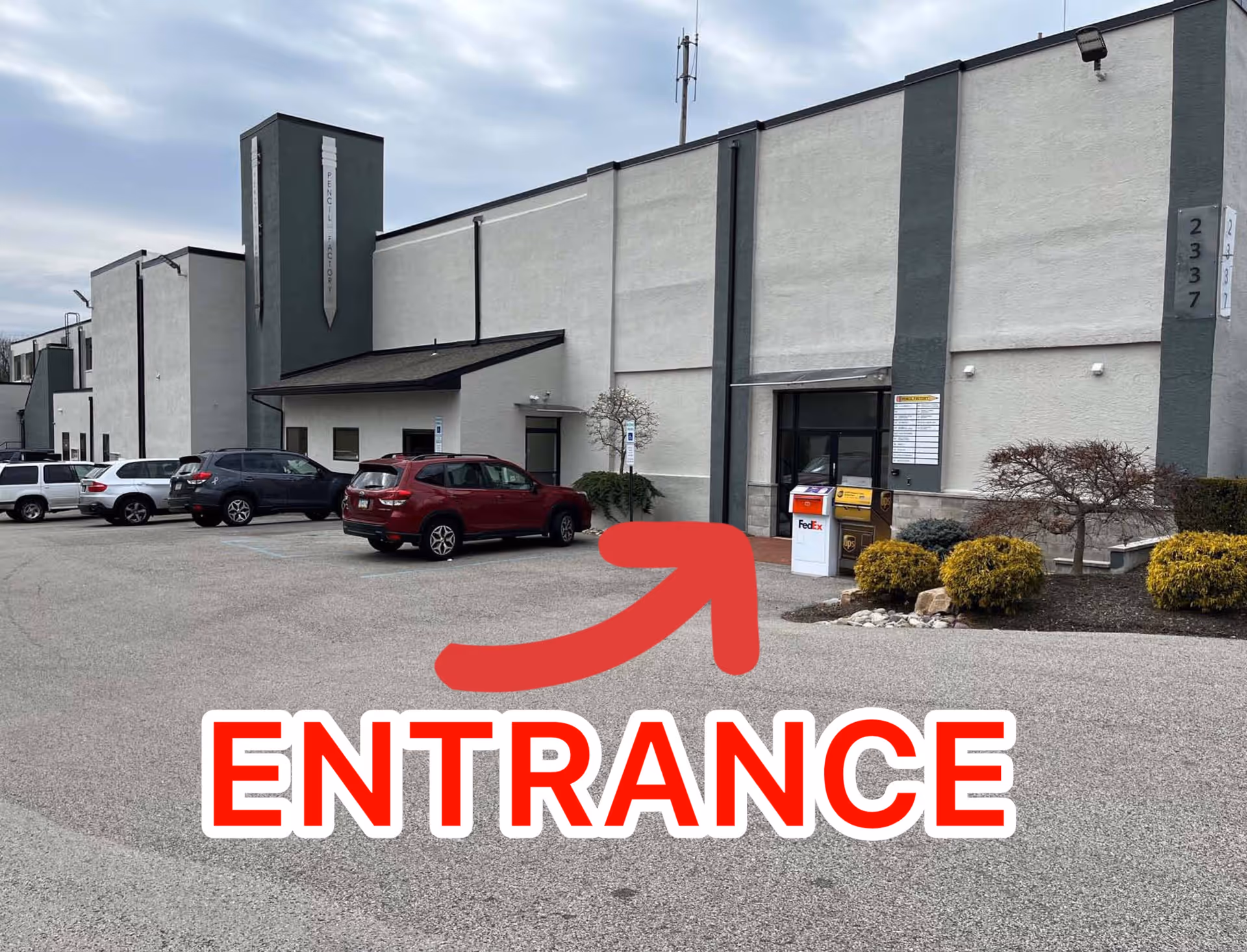 Exterior view of a gray building with a parking lot and marked entrance.