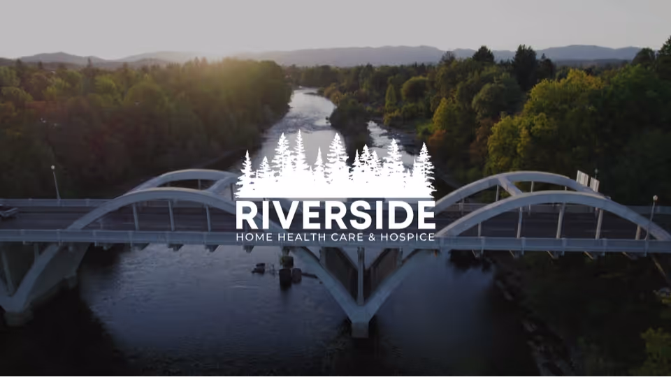 Aerial view of a curved bridge over a river with trees, featuring Riverside logo.