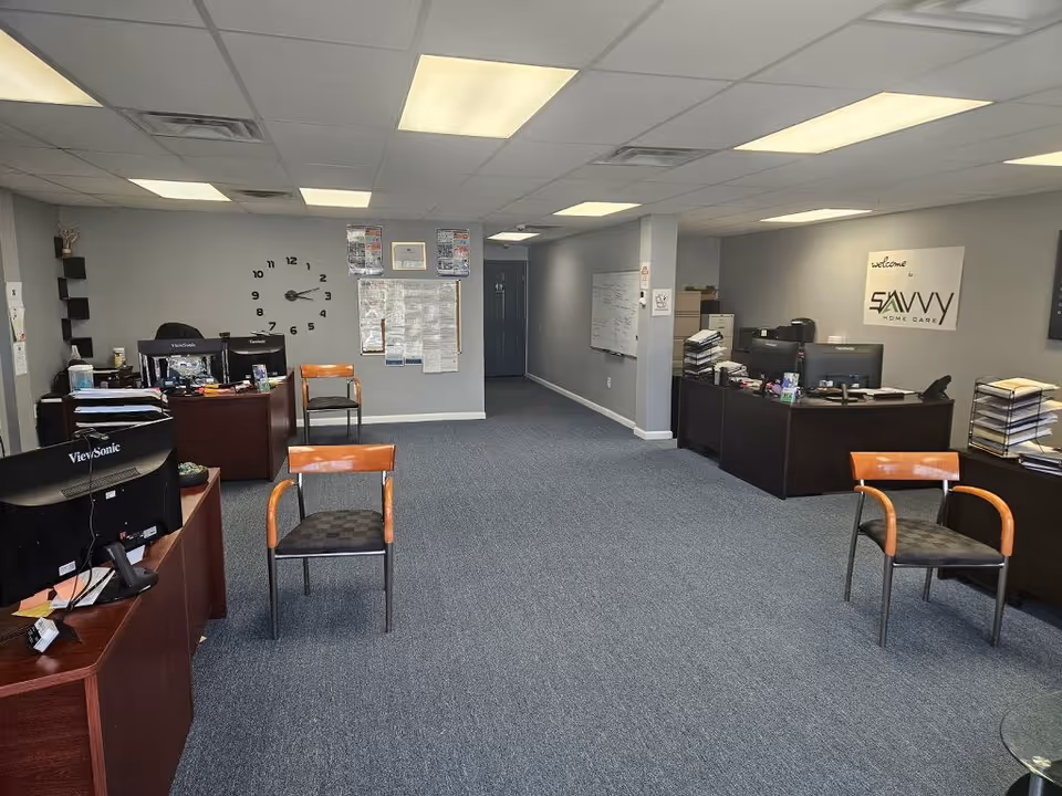 Office reception area with desks, computers, chairs, and a Savvy Home Care sign.