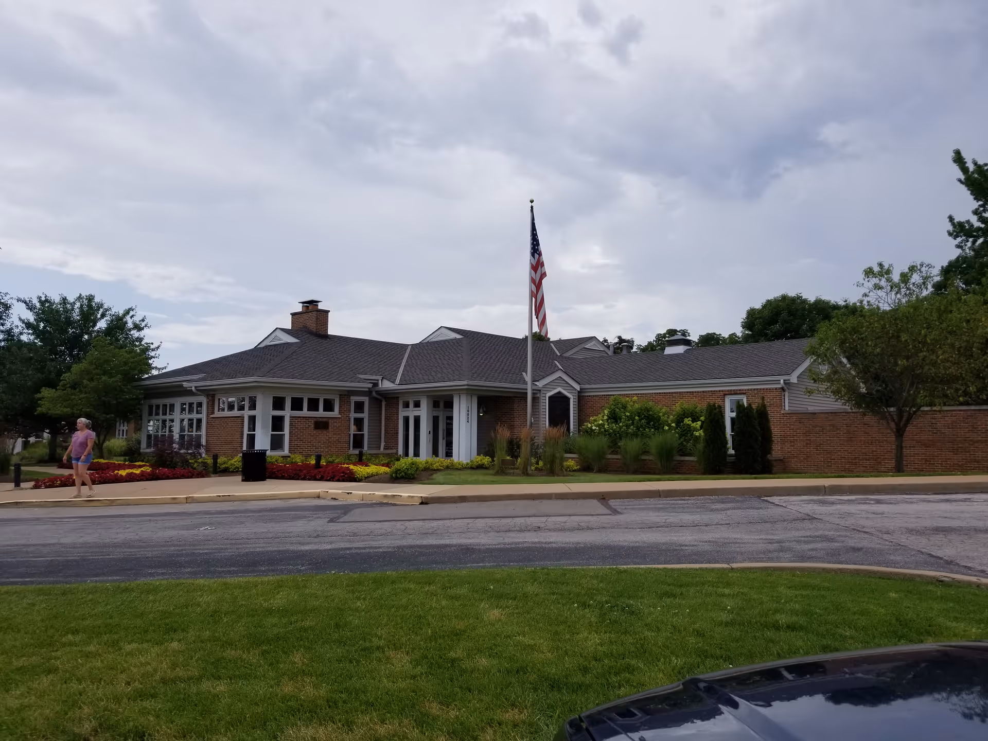 Single-story brick hospice building with flagpole, manicured landscaping, and a person walking nearby