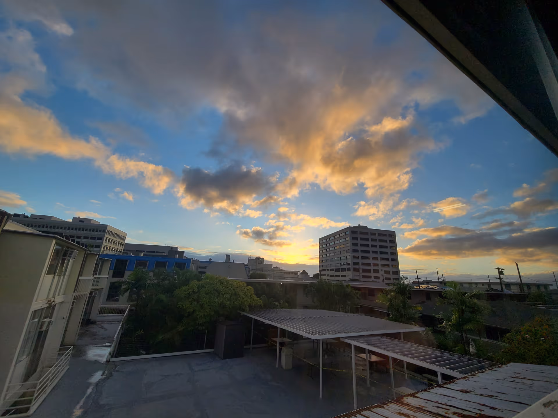 Sunset over a cityscape with rooftops and clouds from a high-rise view.