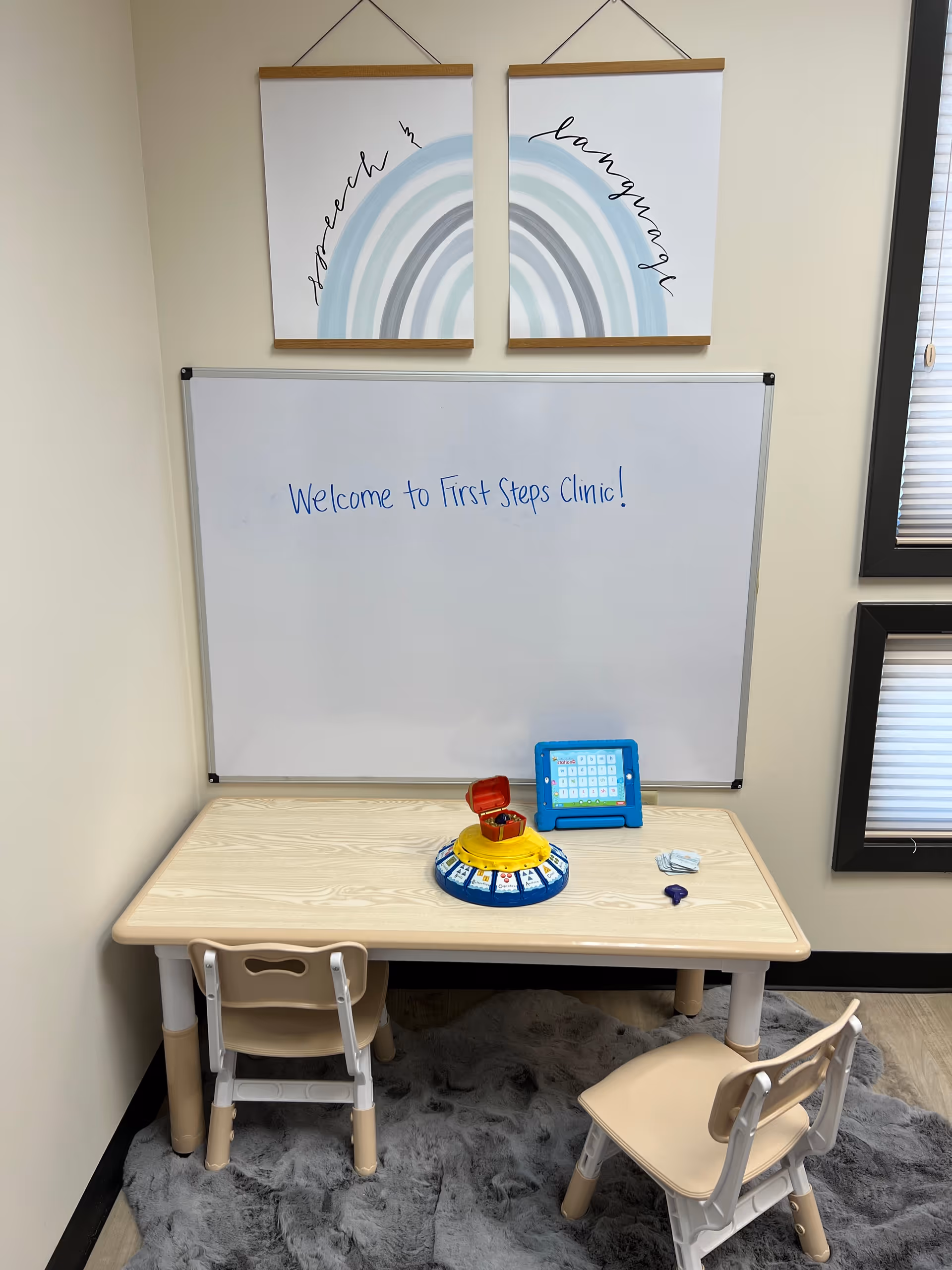 Pediatric therapy play area with child-sized table, chairs, whiteboard, and rainbow artwork.