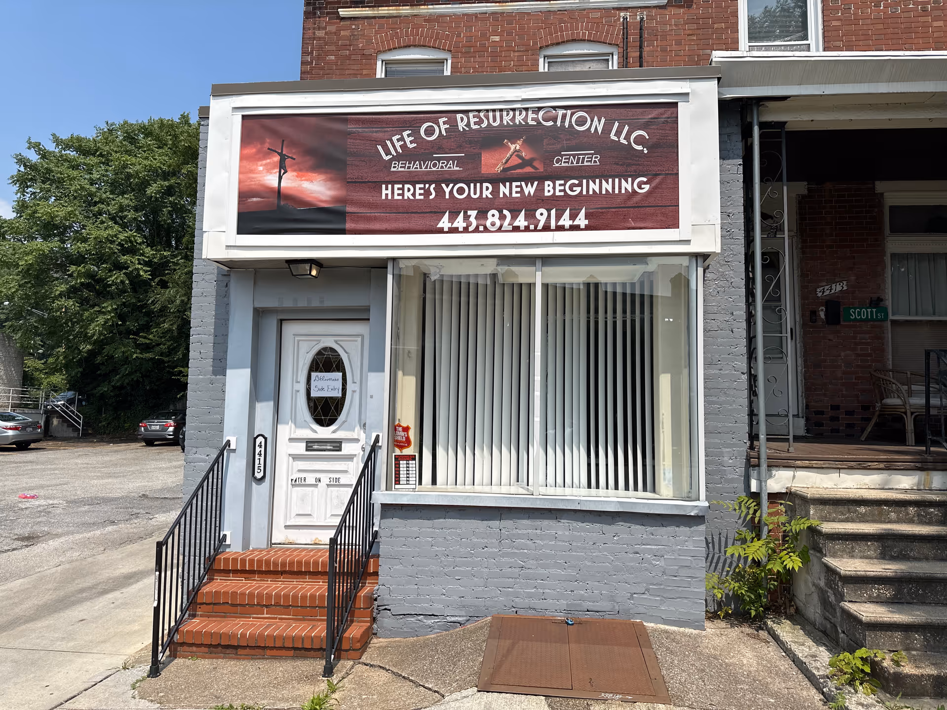 Small storefront with Life of Resurrection LLC sign, doorway, large window, brick exterior, steps.