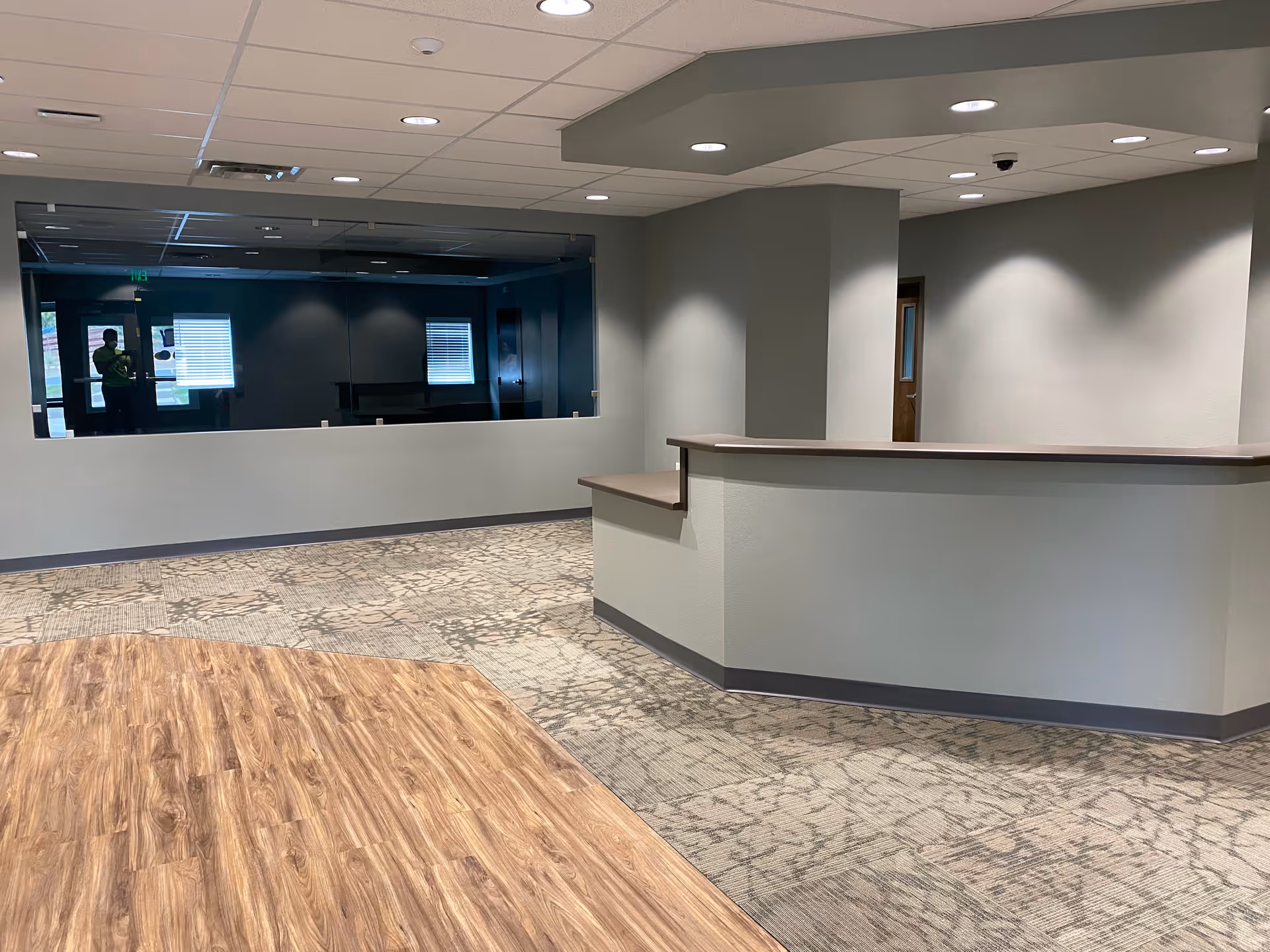 Wide lobby with curved reception desk, wood floor, and soft gray walls.