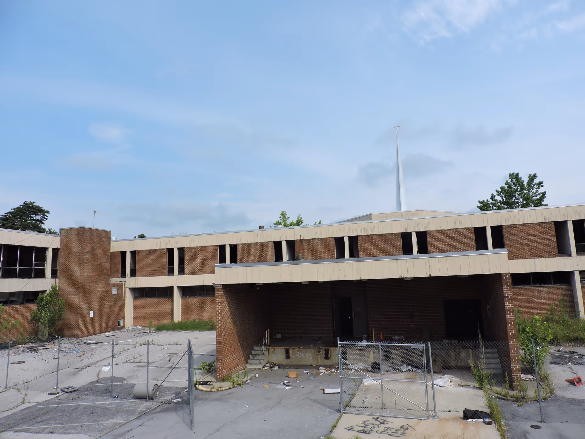 Abandoned brick senior facility exterior with a fenced, debris-filled parking area.