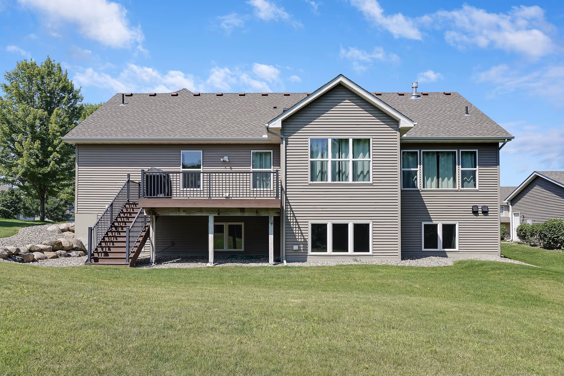 Two-story gray siding house with a deck, stairs, and expansive lawn.