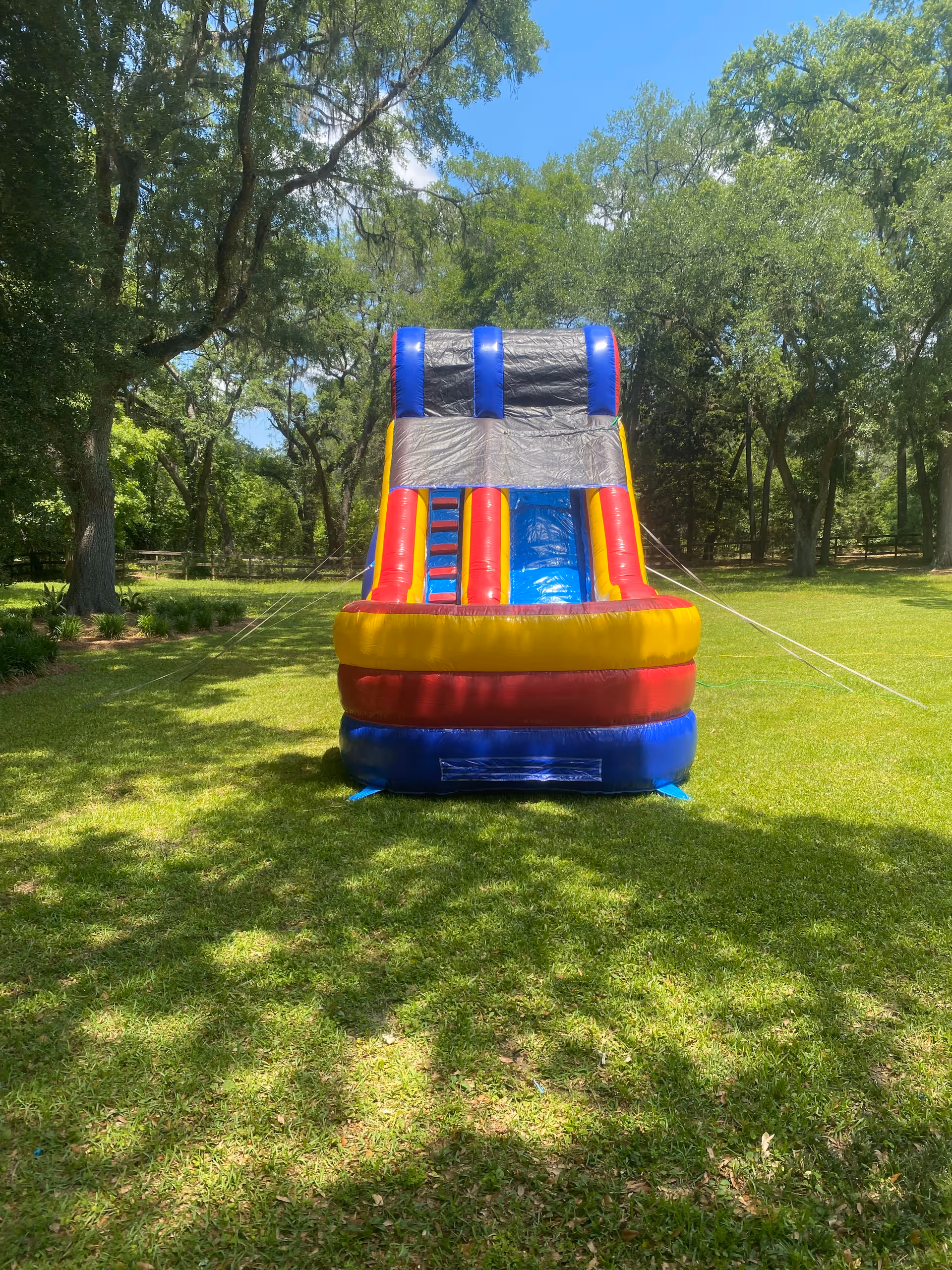 Colorful inflatable bounce house on a grassy outdoor area surrounded by trees.