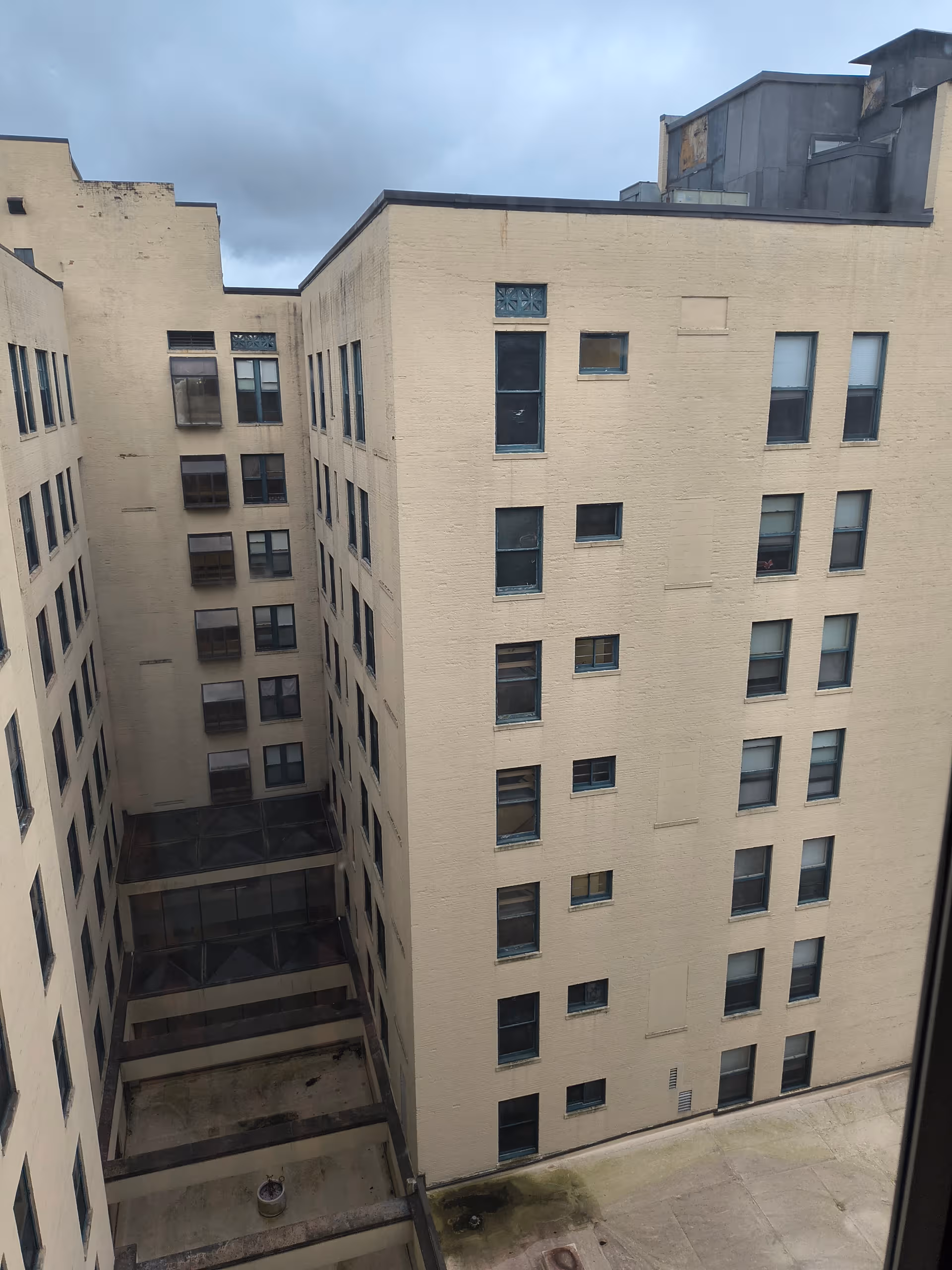 Tall beige apartment building with many windows surrounding a concrete courtyard.