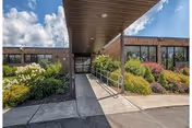 Entrance to Alpine Rehabilitation & Nursing Center: brick exterior, covered walkway, and landscaped shrubs.