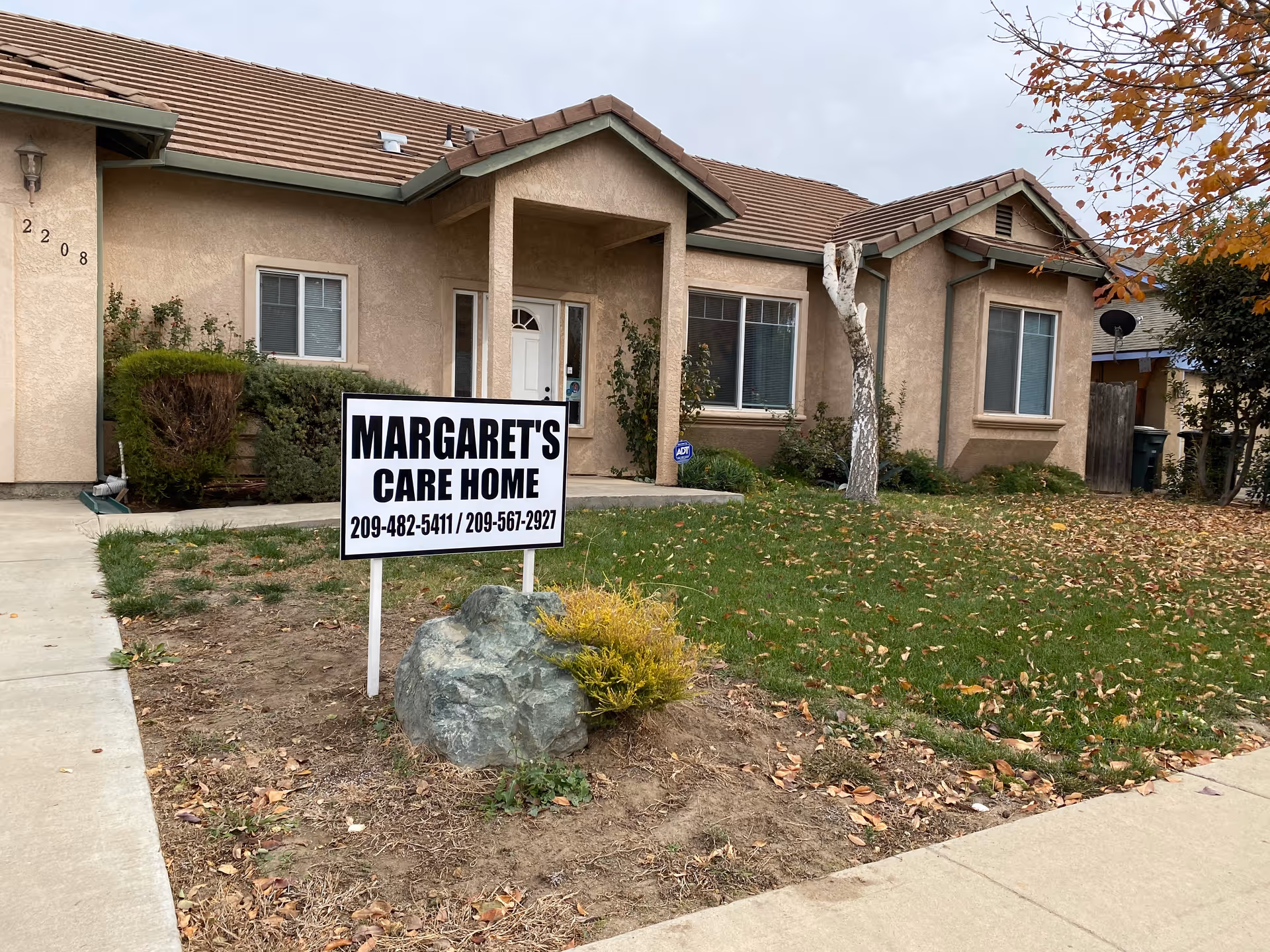 Single-story beige care home exterior with large front-yard sign reading MARGARET'S CARE HOME.