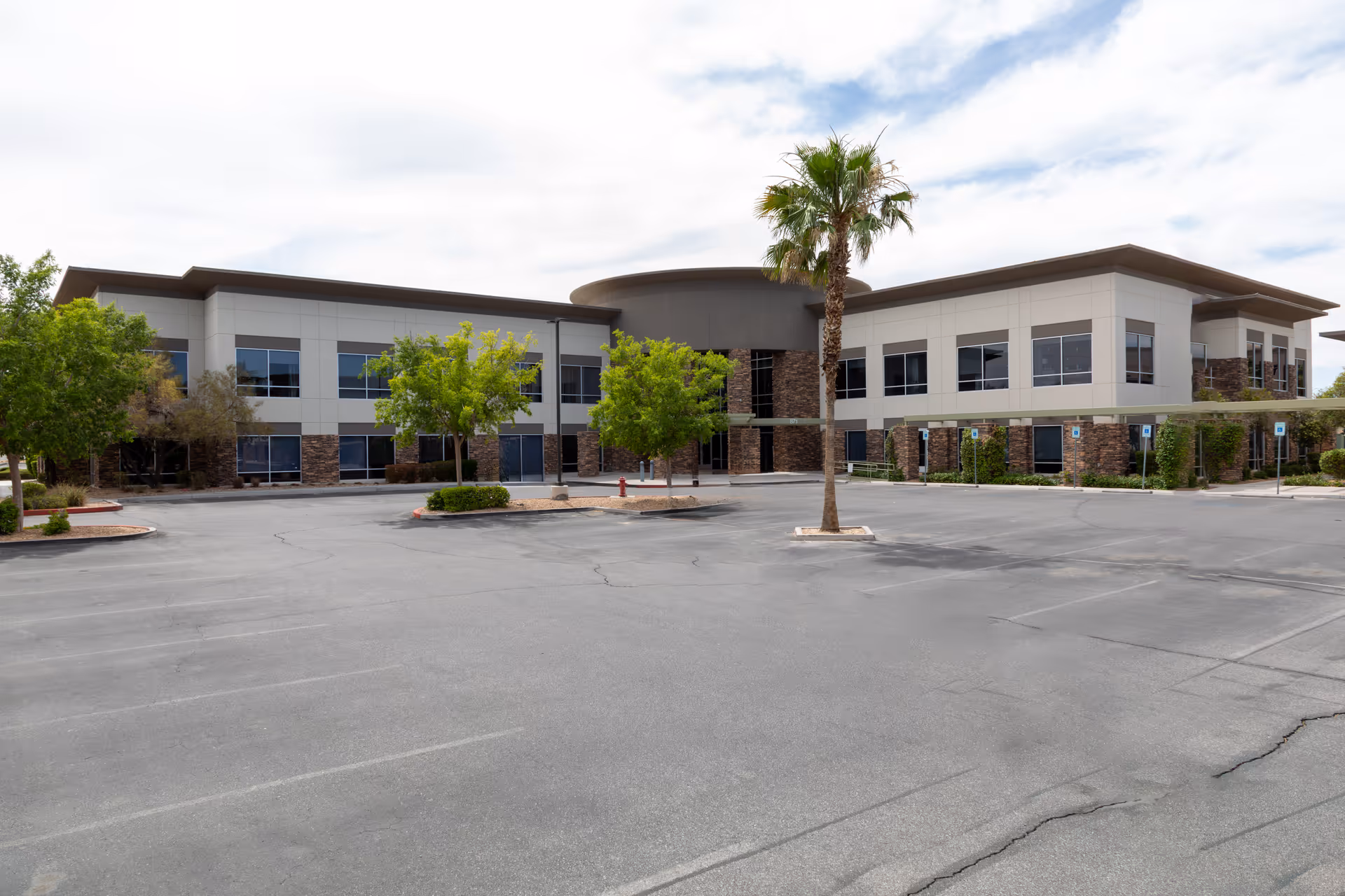Exterior view of a modern medical facility with a curved entrance and parking lot.
