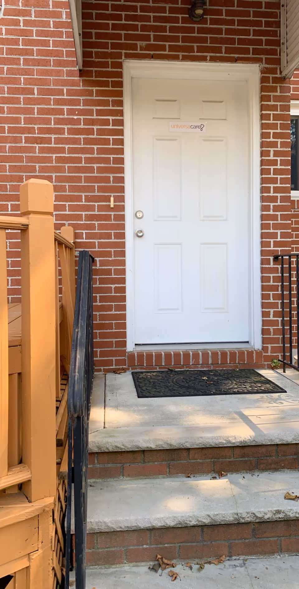 Brick building exterior with a white front door and wooden stairs to a porch.