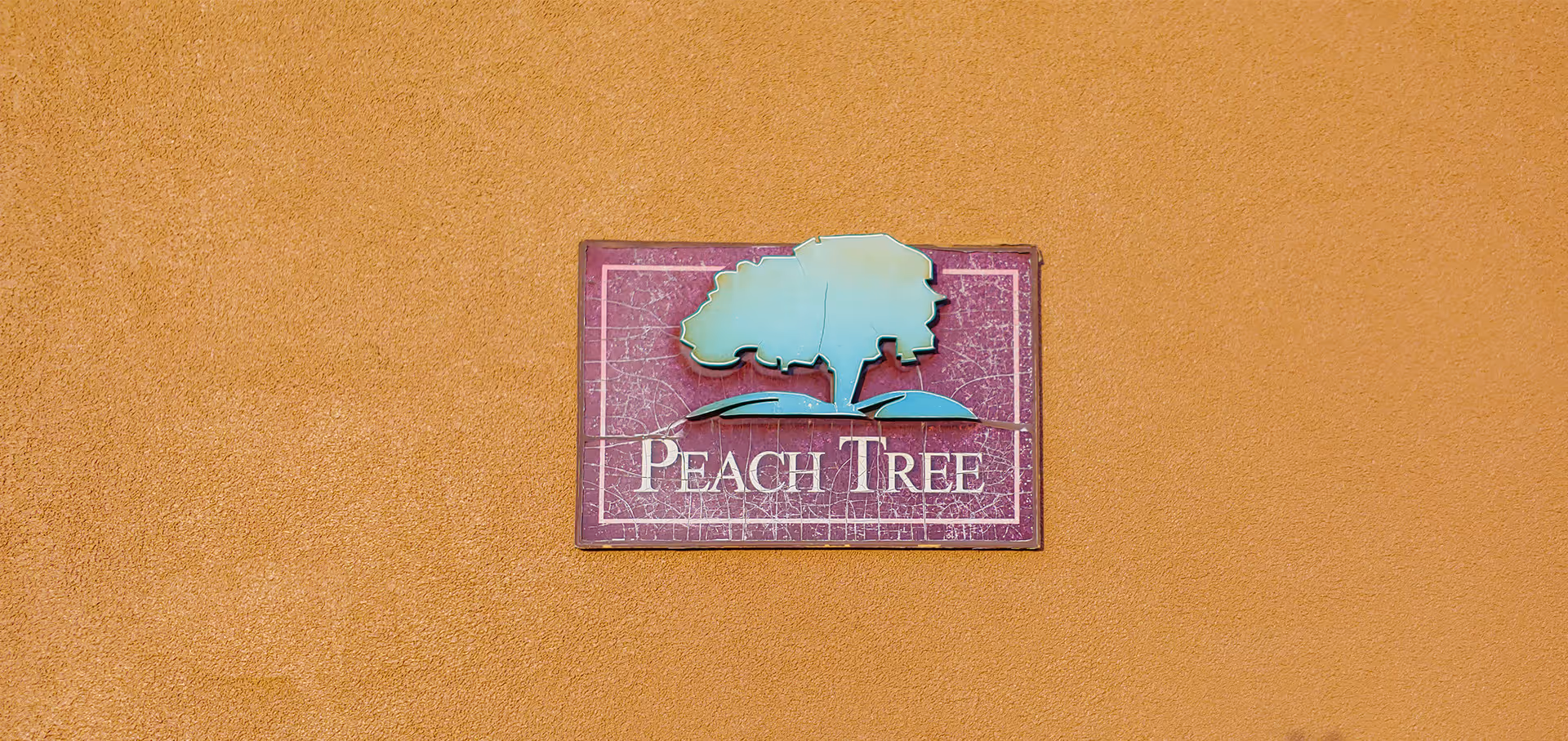 A rectangular 'Peach Tree' sign with a tree logo mounted on a textured orange exterior wall.