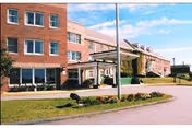 Brick senior living facility with a covered entrance, driveway, and well-kept lawn.