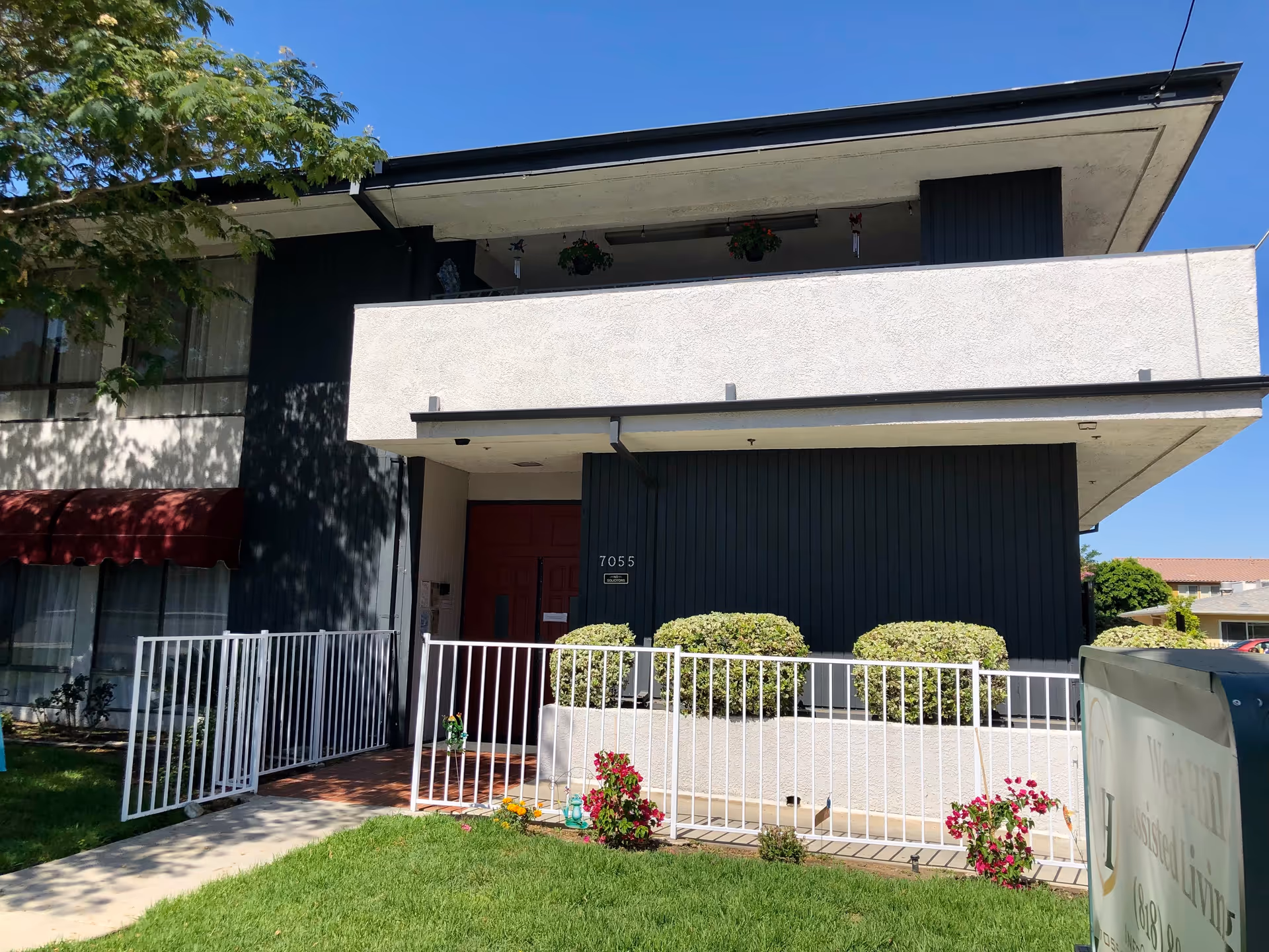 Exterior of a senior living facility with a white fence and red entry door.