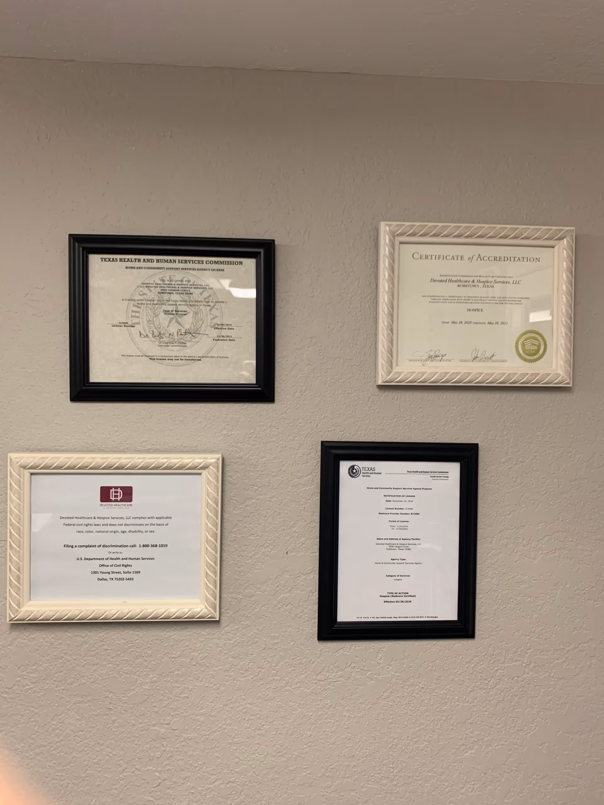 Wall with four framed certificates hanging on a neutral interior wall.