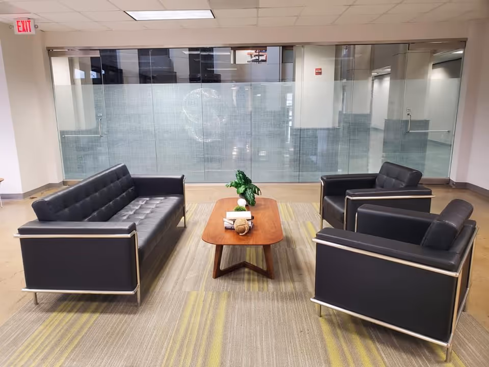 Modern lounge with black leather sofas surrounding a wooden coffee table inside a facility.