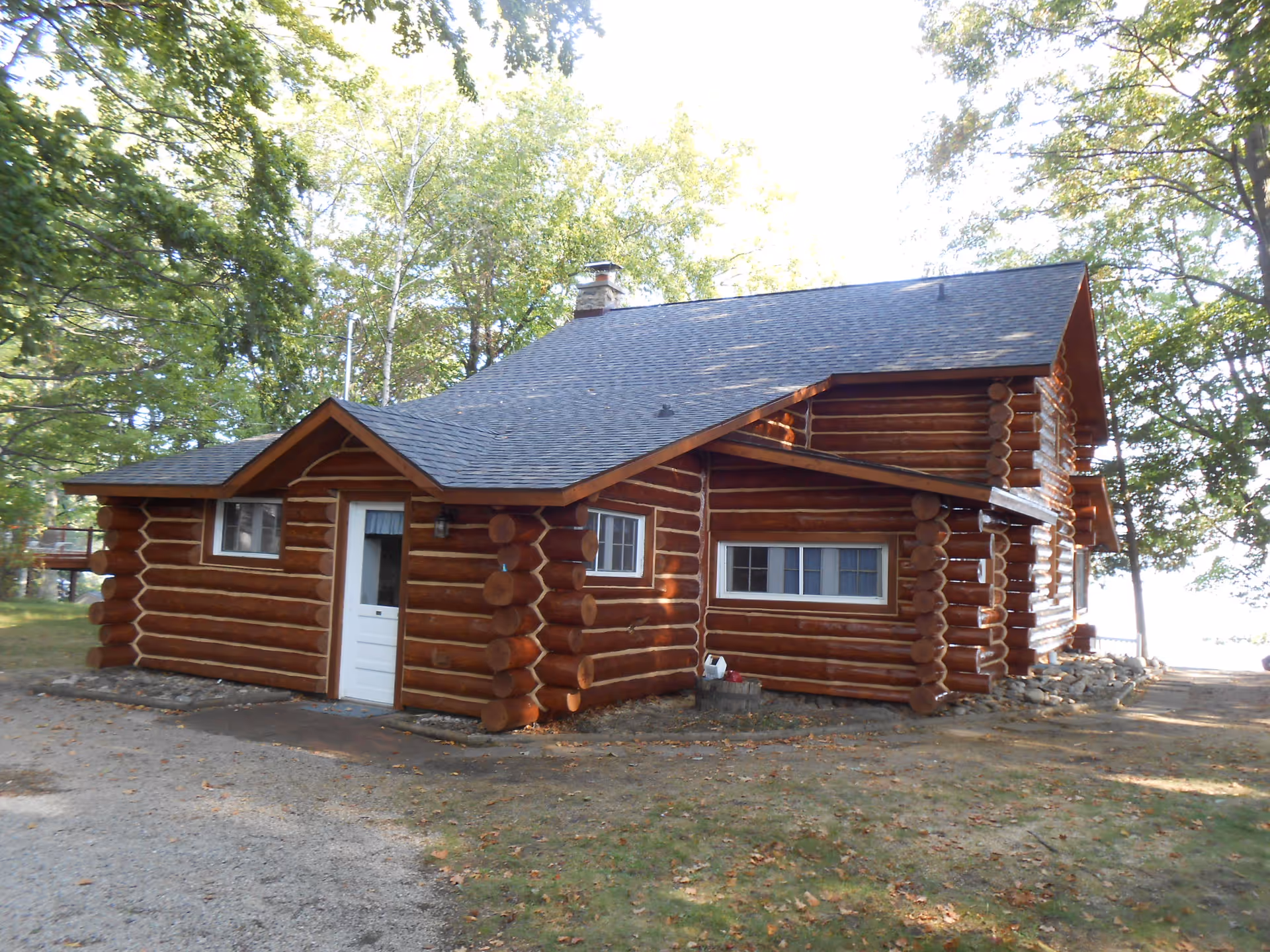 Rustic log cabin style building sits among trees with a gravel driveway.