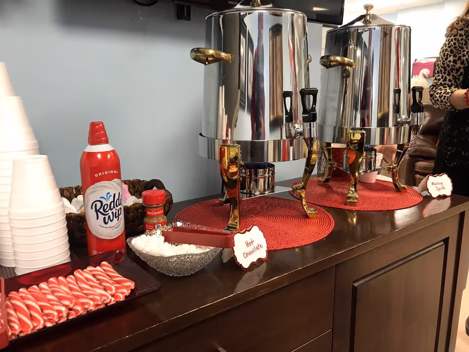 Two shiny beverage dispensers on a dark counter with cups, toppings, and red-striped straws.