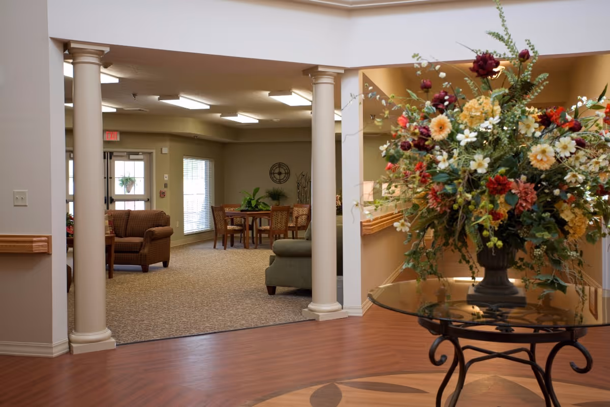 Bright interior common area with a large floral arrangement on a glass table, columns, and seating in the background.