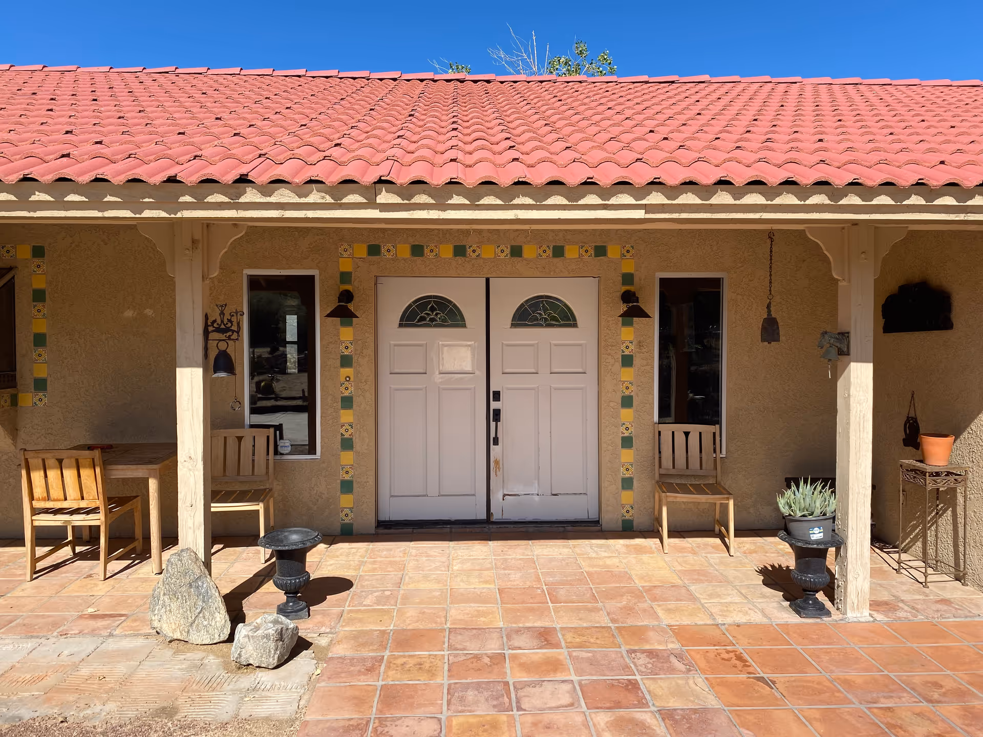 Front entrance of a senior living facility with tiled porch, chairs, and potted plants.